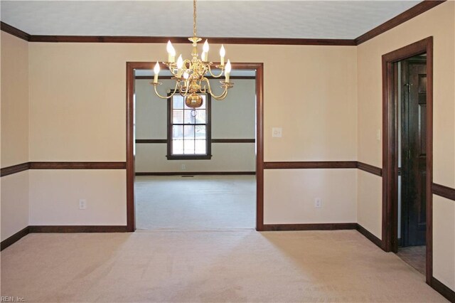 spare room with baseboards, a notable chandelier, ornamental molding, and carpet