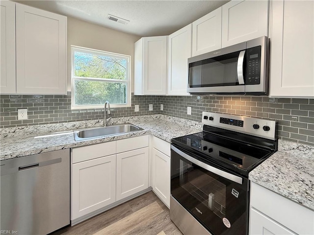 kitchen featuring white cabinetry, a sink, visible vents, light wood-style flooring, and appliances with stainless steel finishes