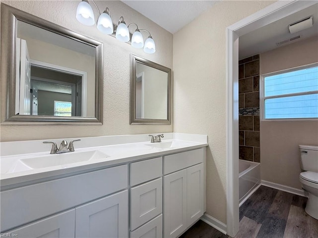 bathroom with visible vents, double vanity, toilet, wood finished floors, and a sink