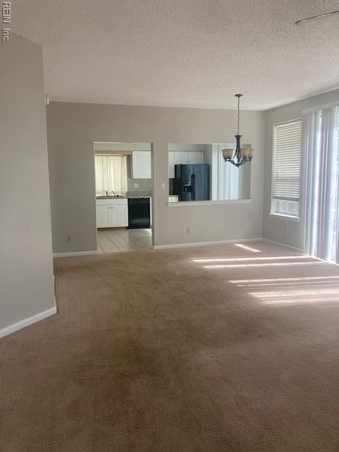 spare room with a sink, a textured ceiling, baseboards, light colored carpet, and an inviting chandelier