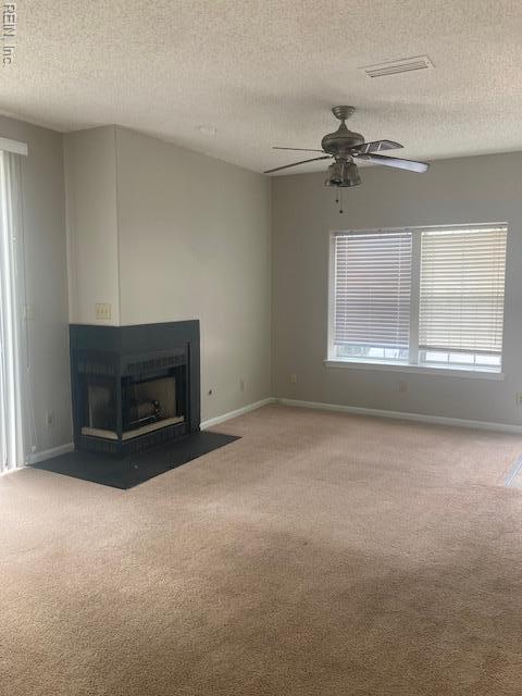 unfurnished living room featuring a fireplace with flush hearth, baseboards, carpet flooring, and a ceiling fan
