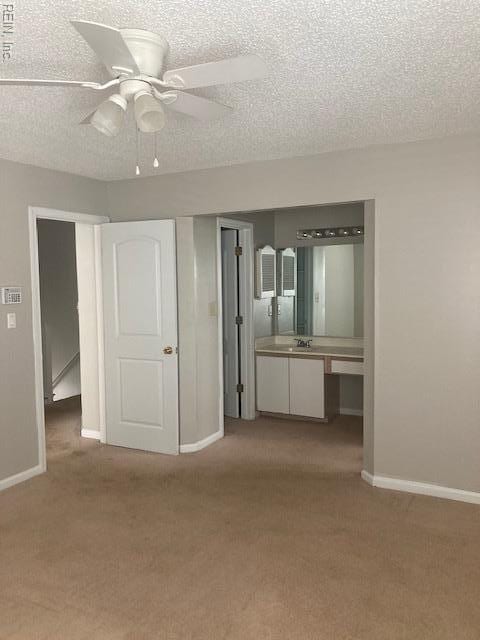 carpeted spare room with baseboards, a ceiling fan, a sink, and a textured ceiling