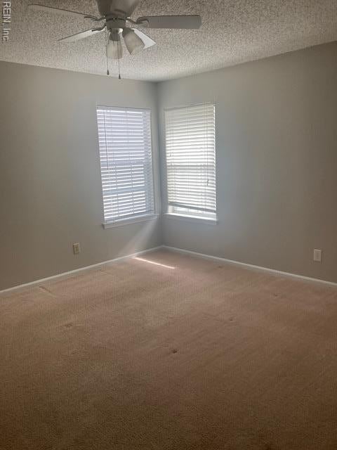 carpeted spare room featuring baseboards, a textured ceiling, and a ceiling fan