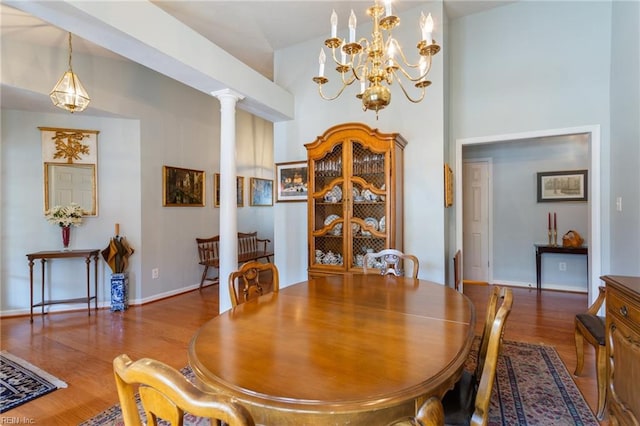 dining area with decorative columns, a chandelier, a high ceiling, wood finished floors, and baseboards