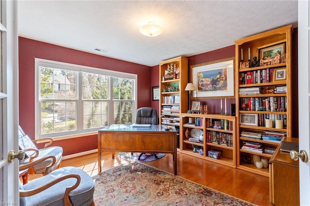 office area with baseboards, visible vents, wood finished floors, and a textured ceiling