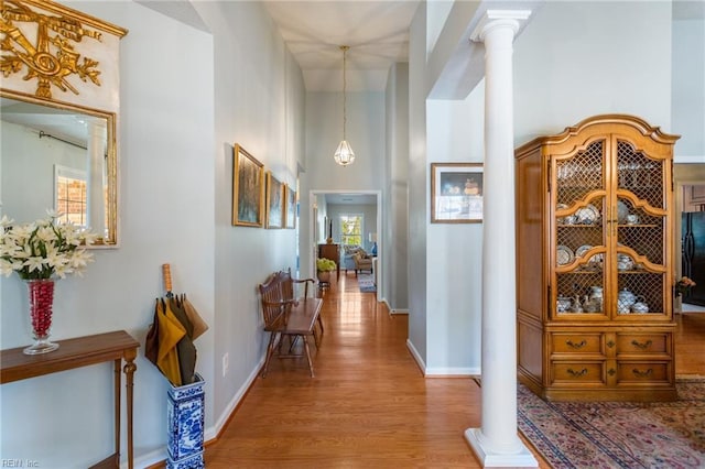 hall with ornate columns, baseboards, a towering ceiling, and wood finished floors