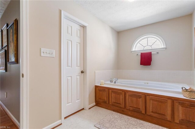 bathroom with a textured ceiling, baseboards, and a garden tub