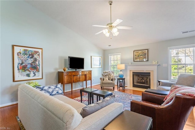 living area with a ceiling fan, a fireplace with flush hearth, wood finished floors, baseboards, and visible vents