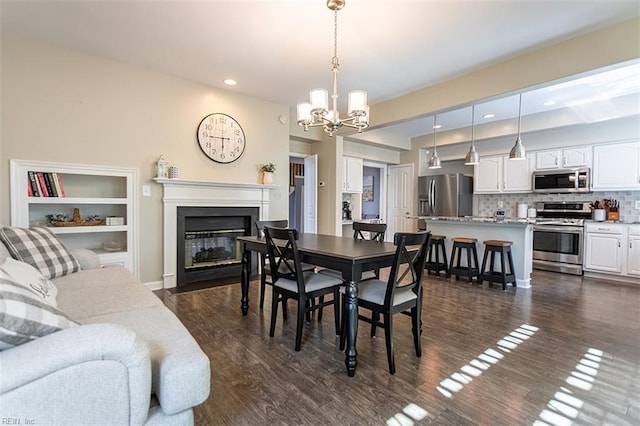 dining room with dark wood-style flooring, a notable chandelier, a glass covered fireplace, and recessed lighting