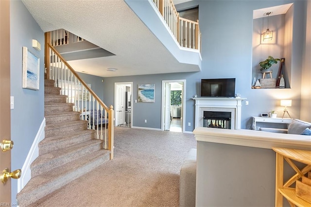 living room with stairway, baseboards, a textured ceiling, carpet floors, and a glass covered fireplace