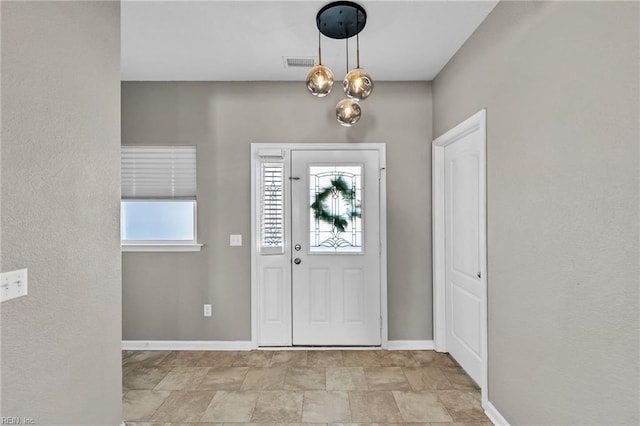 entrance foyer with a chandelier, stone finish floor, baseboards, and visible vents