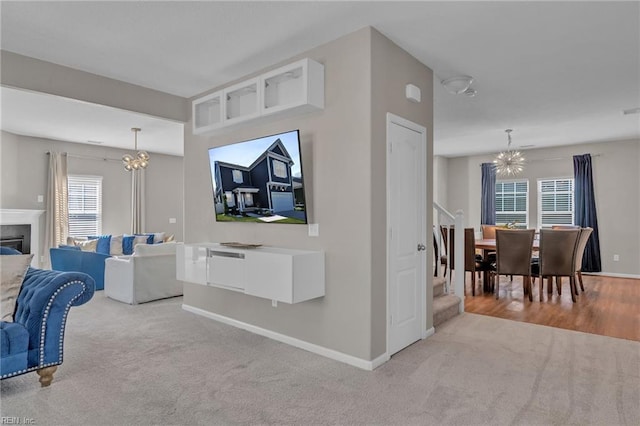 living area with a glass covered fireplace, a notable chandelier, baseboards, carpet floors, and visible vents