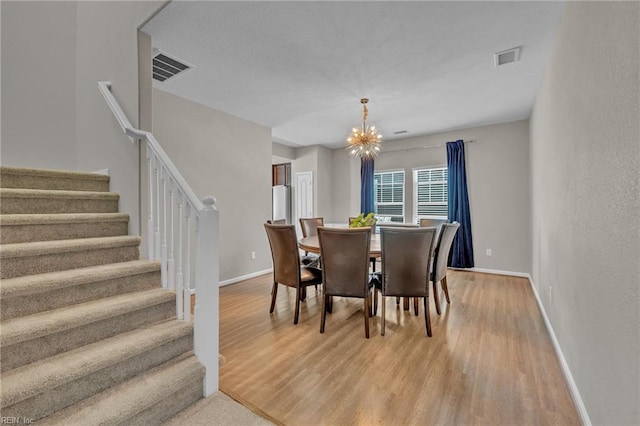 dining area with a chandelier, light wood-style floors, visible vents, and stairway