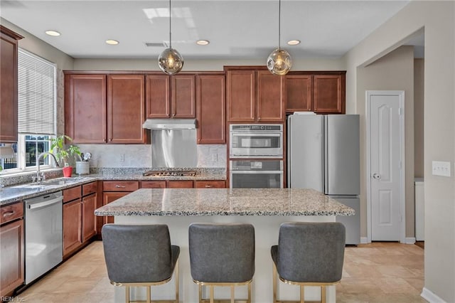 kitchen featuring a sink, under cabinet range hood, light stone countertops, a breakfast bar area, and stainless steel appliances