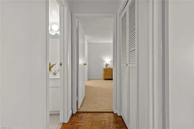 corridor with dark colored carpet, a sink, and baseboards