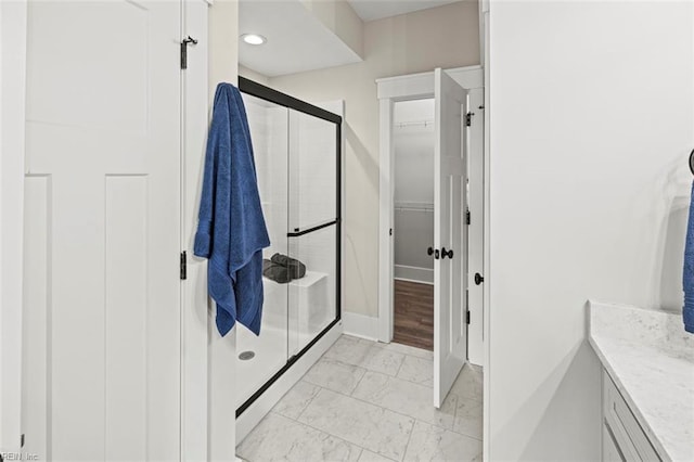 bathroom with a stall shower, vanity, a walk in closet, marble finish floor, and baseboards