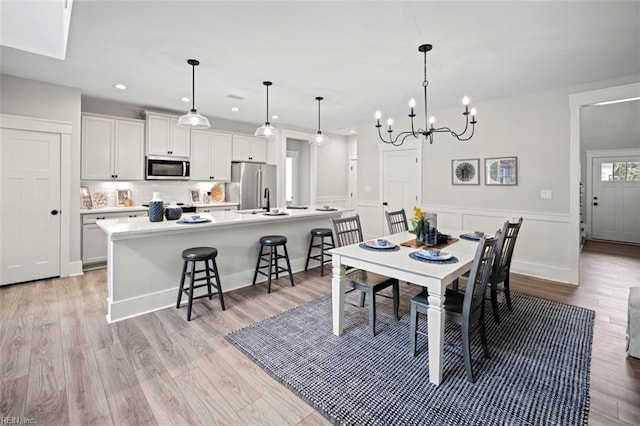 dining space featuring a decorative wall, a chandelier, recessed lighting, light wood-type flooring, and wainscoting