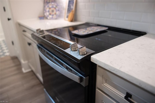 interior details featuring backsplash, light stone countertops, electric range oven, and wood finished floors