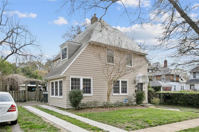 view of property exterior featuring fence, roof with shingles, and a yard