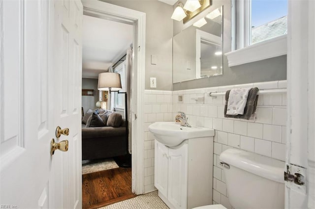ensuite bathroom with tile walls, a wainscoted wall, connected bathroom, toilet, and vanity