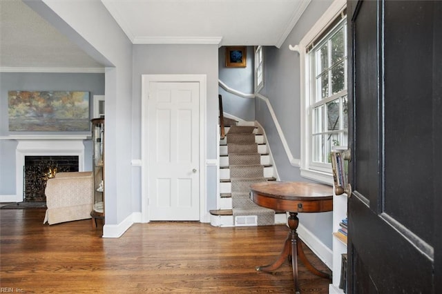 foyer entrance featuring baseboards, crown molding, stairway, and wood finished floors