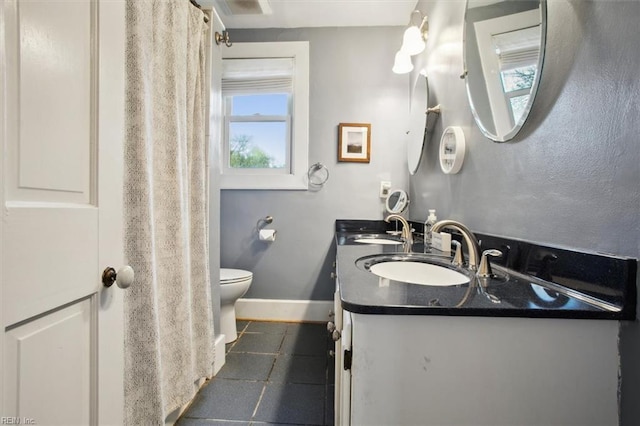 bathroom with baseboards, toilet, double vanity, and a sink
