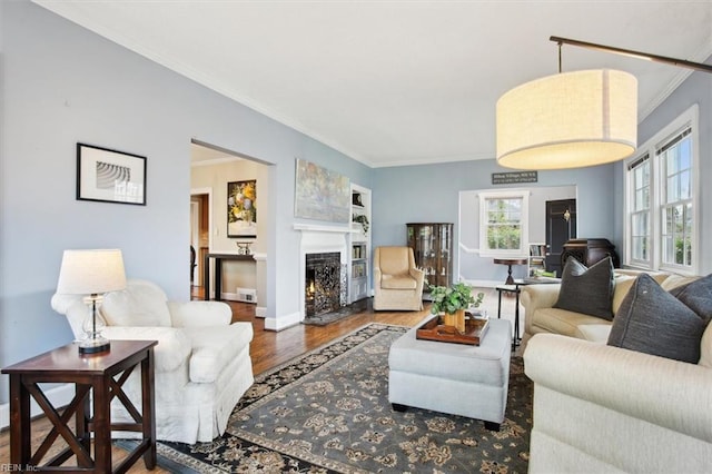 living area featuring a warm lit fireplace, ornamental molding, baseboards, and wood finished floors