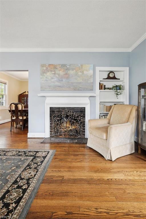 living room featuring built in features, ornamental molding, a fireplace with flush hearth, and wood finished floors
