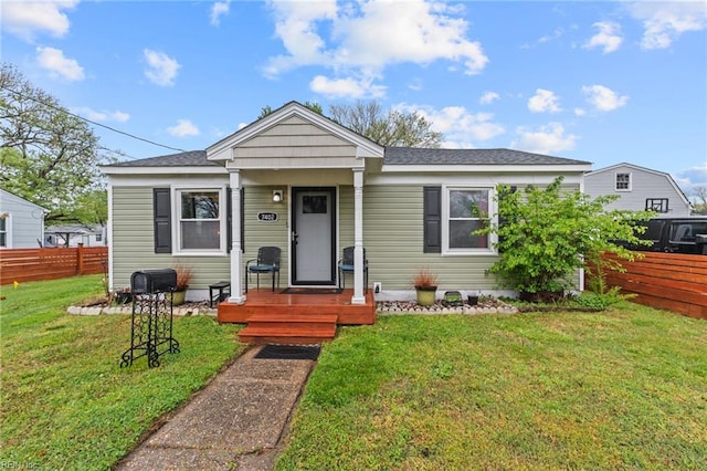 bungalow-style home with a front lawn, fence, and roof with shingles