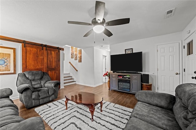 living room featuring a ceiling fan, a barn door, dark wood-style flooring, stairs, and baseboards