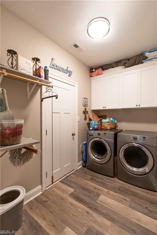 laundry area featuring wood finished floors, baseboards, independent washer and dryer, visible vents, and cabinet space