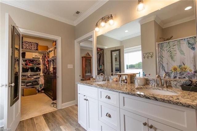 full bath featuring double vanity, a sink, crown molding, and wood finished floors
