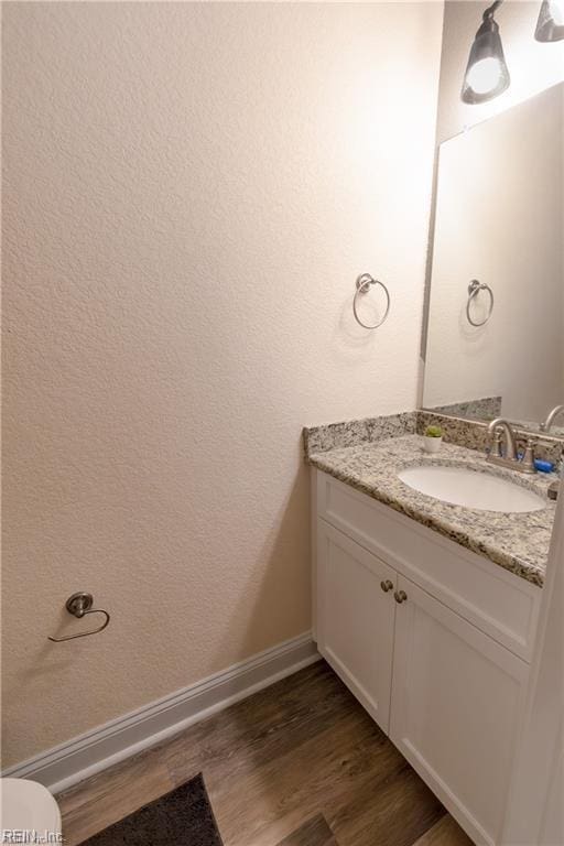 half bath featuring baseboards, wood finished floors, and vanity