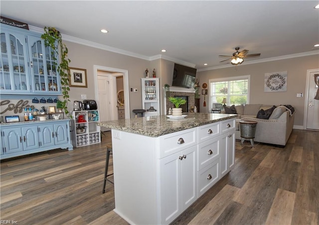 kitchen with a ceiling fan, a fireplace, a center island, dark wood-style floors, and glass insert cabinets