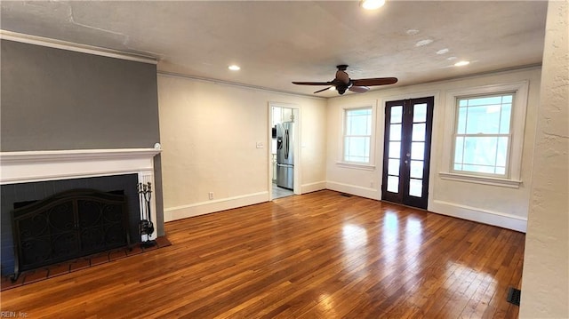 unfurnished living room featuring hardwood / wood-style flooring, a fireplace, ornamental molding, a ceiling fan, and french doors