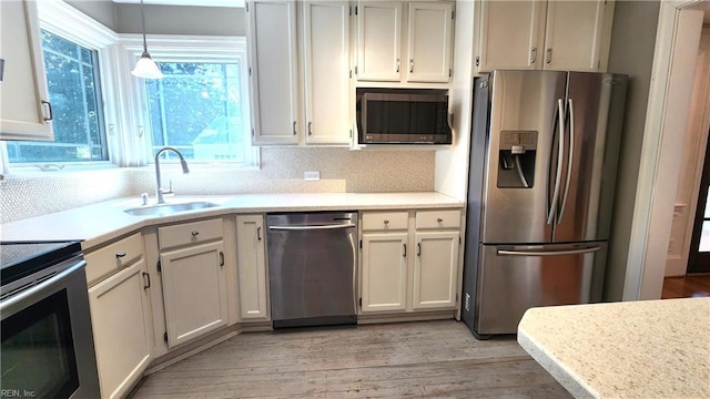 kitchen featuring light countertops, tasteful backsplash, stainless steel appliances, a sink, and light wood-style floors