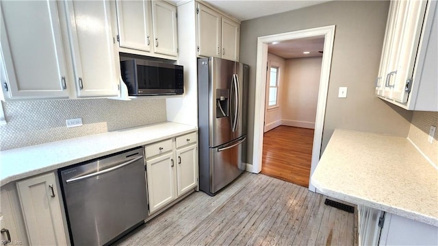 kitchen featuring backsplash, white cabinetry, light wood-style flooring, stainless steel appliances, and baseboards