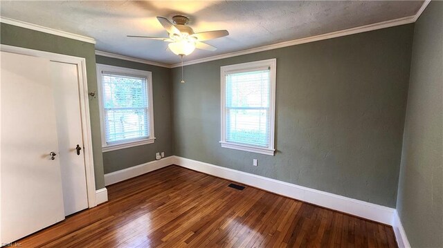unfurnished room with a wealth of natural light, visible vents, crown molding, and wood finished floors