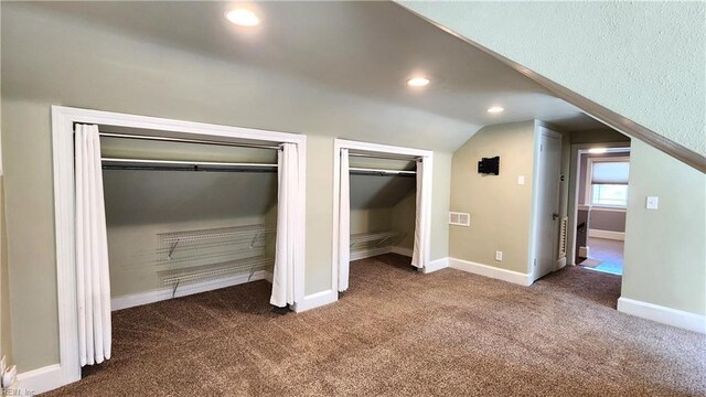unfurnished bedroom featuring vaulted ceiling, dark colored carpet, baseboards, visible vents, and two closets