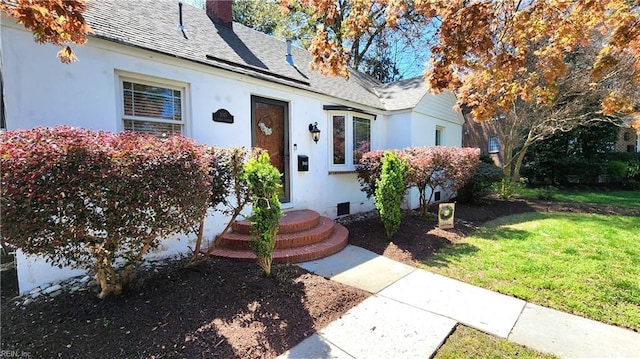 view of front of property featuring stucco siding, roof with shingles, roof mounted solar panels, a front lawn, and a chimney