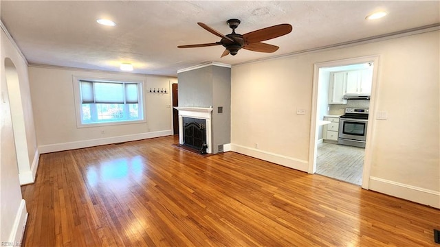 unfurnished living room featuring crown molding, light wood-style floors, a ceiling fan, a fireplace with flush hearth, and arched walkways