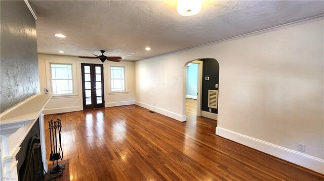 unfurnished living room featuring a textured ceiling, baseboards, ceiling fan, arched walkways, and hardwood / wood-style floors