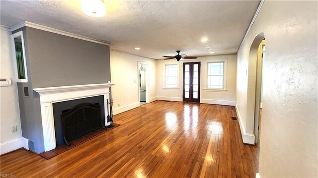 unfurnished living room with crown molding, ceiling fan, a fireplace, arched walkways, and hardwood / wood-style floors