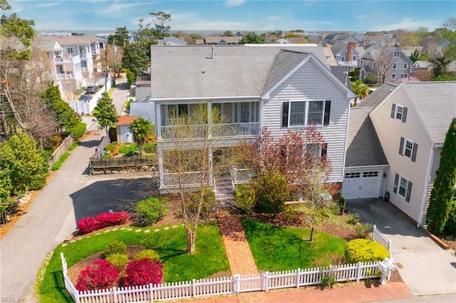view of front of house featuring driveway, a shingled roof, a fenced front yard, and a residential view