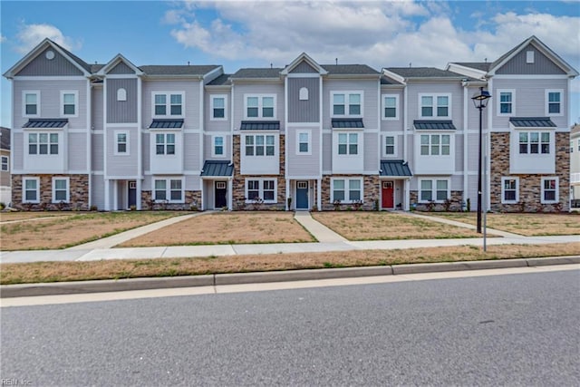townhome / multi-family property featuring a standing seam roof, metal roof, stone siding, a residential view, and a front yard