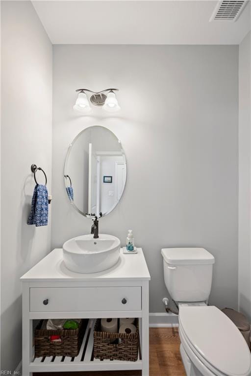 bathroom with toilet, vanity, wood finished floors, baseboards, and visible vents