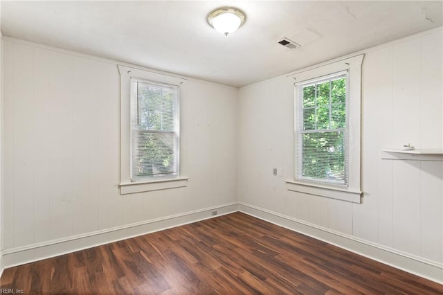 spare room featuring baseboards, a wealth of natural light, dark wood finished floors, and visible vents