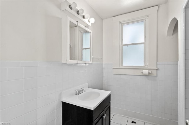 bathroom with a wainscoted wall, tile walls, a healthy amount of sunlight, and vanity