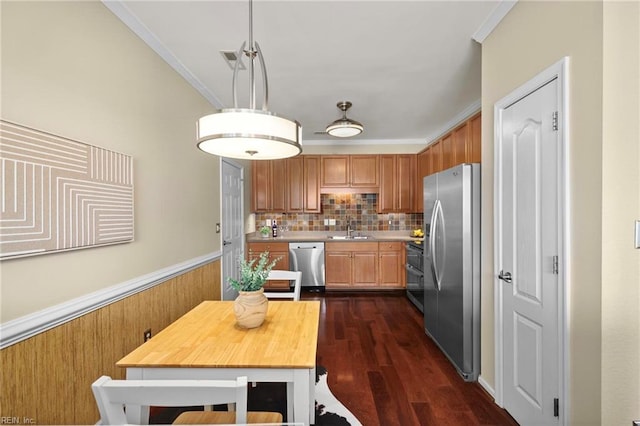 kitchen with light countertops, ornamental molding, appliances with stainless steel finishes, a sink, and wainscoting