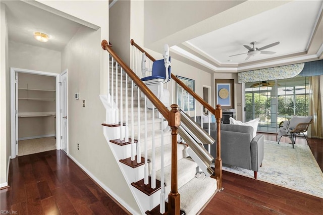 stairs with hardwood / wood-style floors, ornamental molding, baseboards, a raised ceiling, and ceiling fan